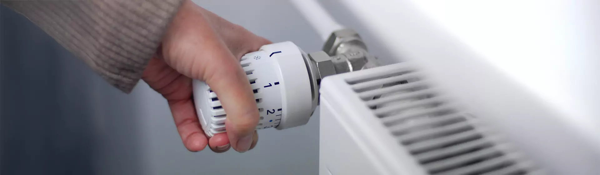 Hand am Temperaturregler eines Heizkörpers Weibliche Hand am Temperaturregler eines Heizkörpers, die zum Energie sparen die Temperatur herunterdreht